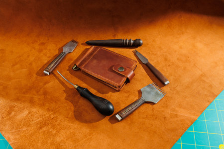 Production of handicrafts from genuine leather. Tools for making leather goods and pieces of brown leather. Production of leather products. View from aboveの写真素材