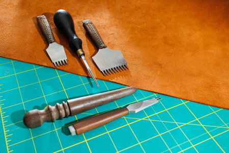 Production of handicrafts from genuine leather. Tools for making leather goods and pieces of brown leather. Production of leather products. View from aboveの写真素材