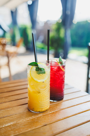 Two glasses of cool refreshing fruit lemonade stand on a wooden table. Summer soft drinks