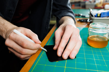 The hands of the master sew handmade leather products. Men's hands connect the parts, creating quality leather accessories. Working process in a leather workshopの写真素材