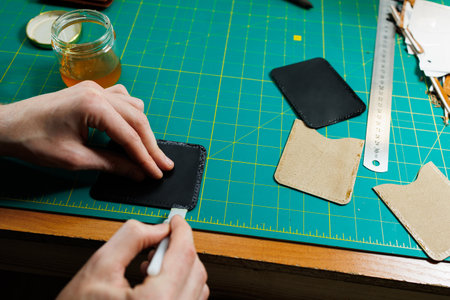 The hands of the master sew handmade leather products. Men's hands connect the parts, creating...