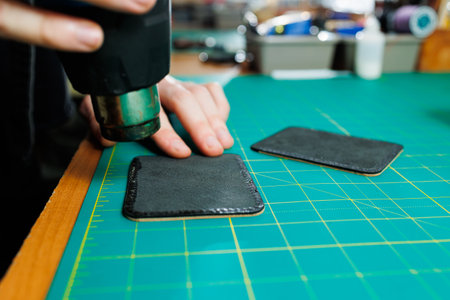 Hands of a professional craftsman make a leather wallet new, clean genuine leather wallet, close-up cropped shot.の写真素材