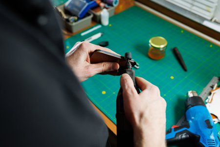 The hands of the master sew handmade leather products. Men's hands connect the parts, creating quality leather accessories. Working process in a leather workshopの写真素材