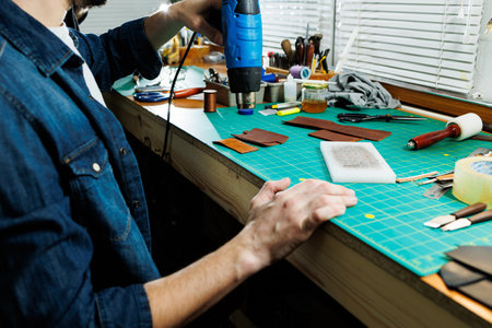 The hands of the master sew handmade leather products. Men's hands connect the parts, creating...