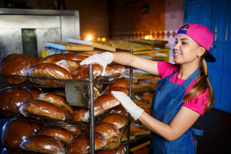 Professional baker - a young pretty woman in a denim apron holds fresh bread in her hands. Bakery...