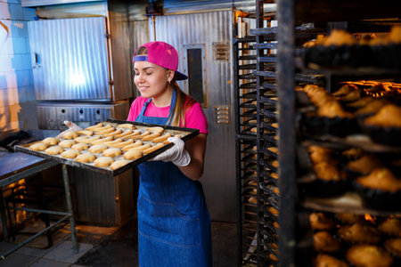 A professional baker girl is holding a tray with fresh cookies in her hands. Sweet pastries in a bakeryの写真素材