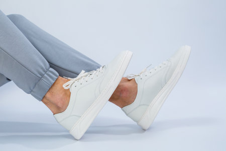 Men's feet in white everyday sneakers made of natural leather on lacing. High quality photo