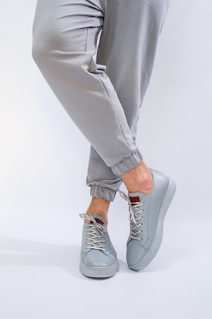 Men's sneakers on a very gray day of natural leather, men's legs shoes in gray leather shoes. High...