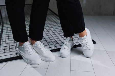 Close-up of male and female legs in black pants and white casual sneakers. Summer men's and women's leather shoesの写真素材