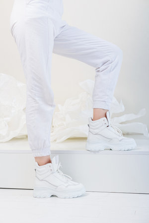 Beautiful female legs in white trousers, white leather sneakers. New collection of women's casual shoesの写真素材