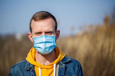 Close up portrait of a man outdoor in a surgical mask with rubber ear straps. Typical three-layer surgical mask for covering the mouth and nose. Bacteria mask procedure. Protection concept.の写真素材