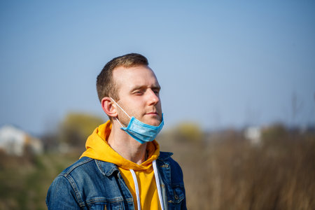 Close up portrait of a man outdoor in a surgical mask with rubber ear straps. Typical three-layer...