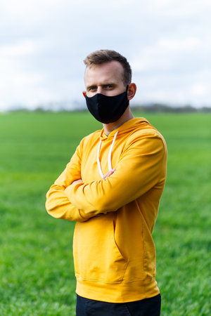 Young man in black protective antiviral mask on the street. The guy is resting in the park on a sunny summer day in a mask made by his own hands. Virus protection. Quarantine measuresの写真素材