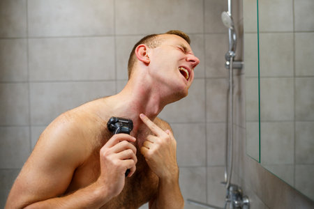 A man shaves his face with an electric razor in front of a mirror. Skin irritation. Bath procedureの写真素材
