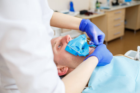 Dentist during the treatment of a male patient. Female dentist in face mask with male patient sitting in dentist chair sitting in dental clinic. Selective focusの写真素材