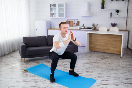 Young man goes in for sports at home, squats in the living room. Healthy lifestyle