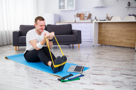 Online training. Man doing exercise with rubber bands at home, free space. Doing sports at home
