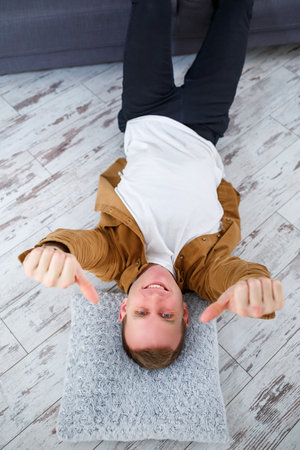 Happy young man lying on the floor near the sofa in the living room and restingの写真素材