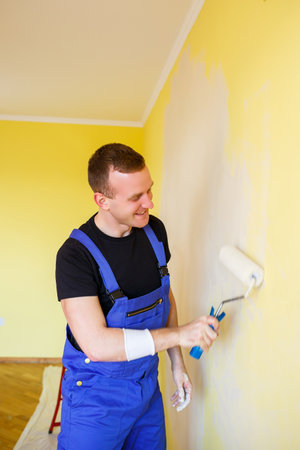 Young man in overalls hold a paint roller. Tools accessories for apartment room renovation. Home renovation conceptの写真素材