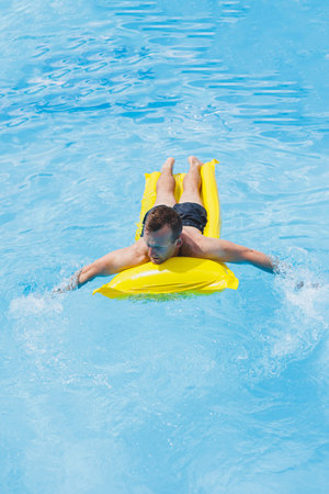 A young man in shorts enjoys the water park floating in an inflatable big ring on a sparkling blue...