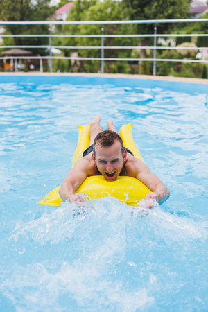 A young man in shorts enjoys the water park floating in an inflatable big ring on a sparkling blue...