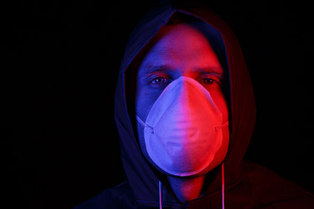A man in a protective rubber suit and a white medical mask. Virus protection. Illuminated in red and blue.の写真素材