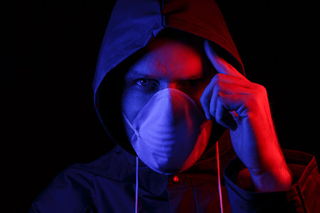 A man in a protective rubber suit and a white medical mask. Virus protection. Illuminated in red and blue.の写真素材