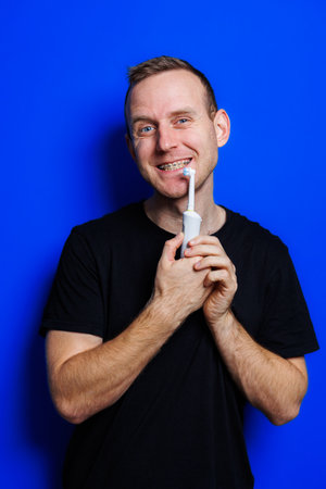 Portrait of a young handsome man brushing his teeth with an ultrasonic modern toothbrush. Oral care....