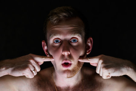 Young man shaving his beard. He shaved off half the bristles against a gray background. Male face...