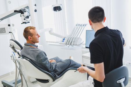 A young dentist doctor tells a male patient about dental care. A man was sitting in a dental chair at a doctor's appointment. Modern dental treatmentの写真素材