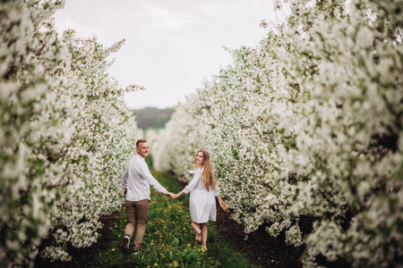 Happy family couple in spring blooming apple orchard. Young couple in love enjoy each other while...
