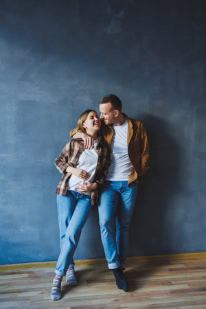 Happy couple in love dressed in shirts, standing on the background of gray wall, looking at empty space, isolated background of gray concrete wall. The concept of a happy couple in love.の写真素材