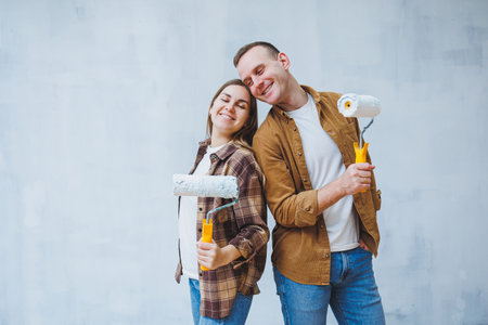A young married couple in love paints the walls with white paint using rollers. Renovation in the apartment of a happy coupleの写真素材