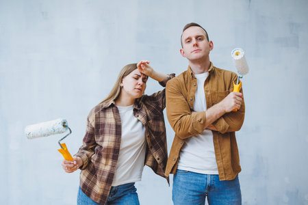 A young married couple in love paints the walls with white paint using rollers. Renovation in the apartment of a happy coupleの写真素材