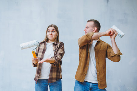 Happy young married couple in love in shirts doing renovations, renovating walls painting with white paint roller, preparing to move into new house, selective focus.の写真素材