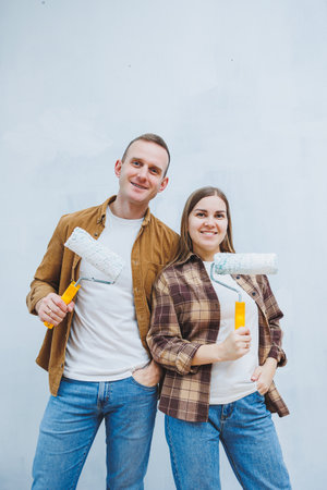 Happy young married couple in love in shirts doing renovations, renovating walls painting with white paint roller, preparing to move into new house, selective focus.の写真素材