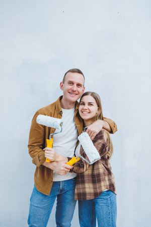 Couple in love, newlyweds in shirts and jeans in an empty room, painting white walls and renovating the interior. A man and a woman moved to a new house. Selective focusの写真素材