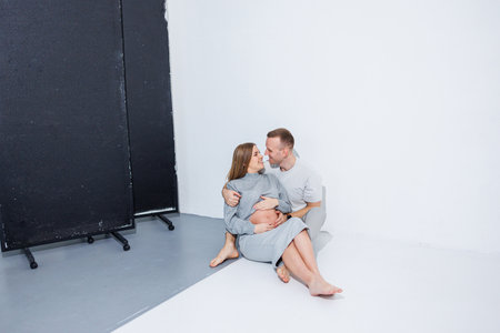 Happy husband and pregnant wife expecting a baby are hugging on a white background. Young happy married couple are happy about pregnancy and hugging.の写真素材