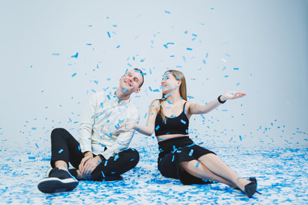 Happy couple laughing at gender party while sitting in blue confetti. Gender partyの写真素材