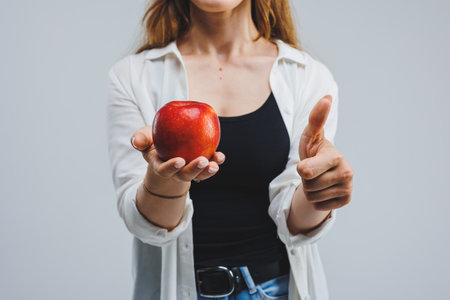 Smiling woman holding a red apple. Beautiful brunette in a white shirt. Healthy plant food and vitamins. White background.の写真素材