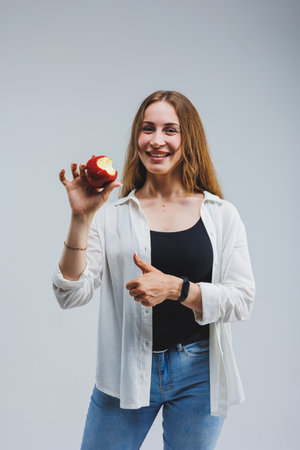 Smiling woman holding a red apple. Beautiful brunette in a white shirt. Healthy plant food and vitamins. White background.の写真素材