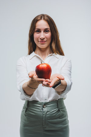 Smiling woman holding a red apple. Beautiful brunette in a white shirt. Healthy plant food and vitamins. White background.の写真素材