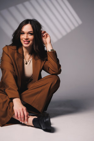 Beautiful elegant young woman model in nice stylish brown suit posing on gray background. Young elegant woman in a suitの写真素材