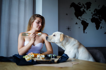 Beautiful girl eating sushi close-up with her dog labrador, smiling, holding a sushi roll with chopsticks. Healthy Japanese food.の写真素材