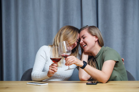 two girls of European appearance with blond hair are sitting at the table, drinking wine and laughing, relaxing at home, alcoholの写真素材