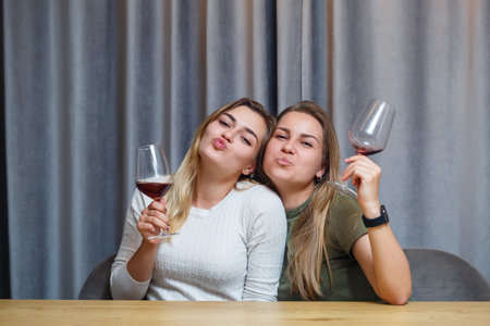 two girls of European appearance with blond hair are sitting at the table, drinking wine and laughing, relaxing at home, alcoholの写真素材