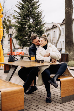 Happy young couple in love in outerwear sitting at a table outside and drinking coffee. Relaxing in the open airの写真素材
