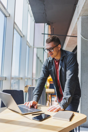 Portrait of a man, IT professional, working remotely with a modern laptop, sitting at a table and smiling at the camera during a break, a happy human programmer in vision correction glassesの写真素材