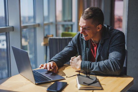 Portrait of a man, IT professional, working remotely with a modern laptop, sitting at a table and...