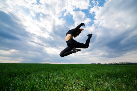 Young professional gymnast is jumping in nature against the blue sky. Girl athlete in a black top...